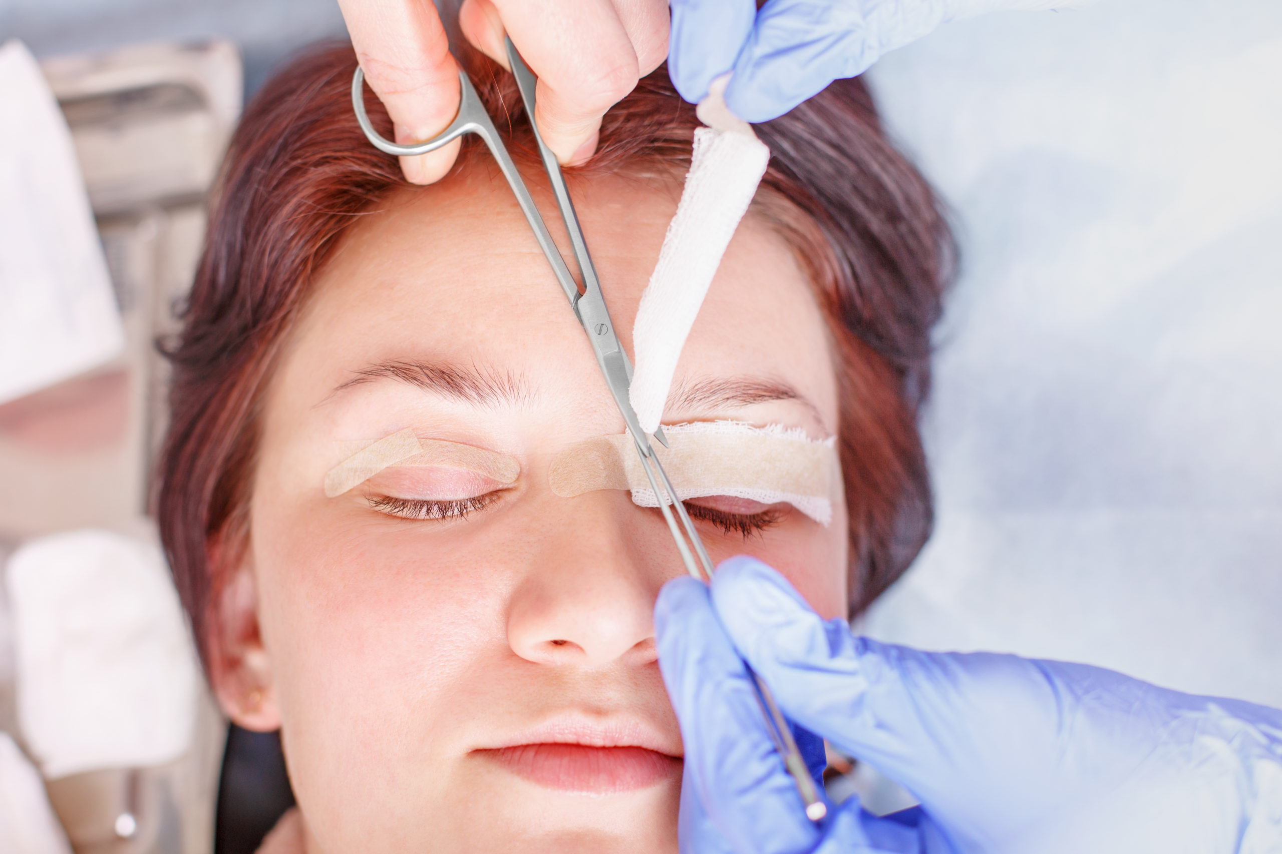 Surgeon applies a bandage to the female patient's eyelids after surgery