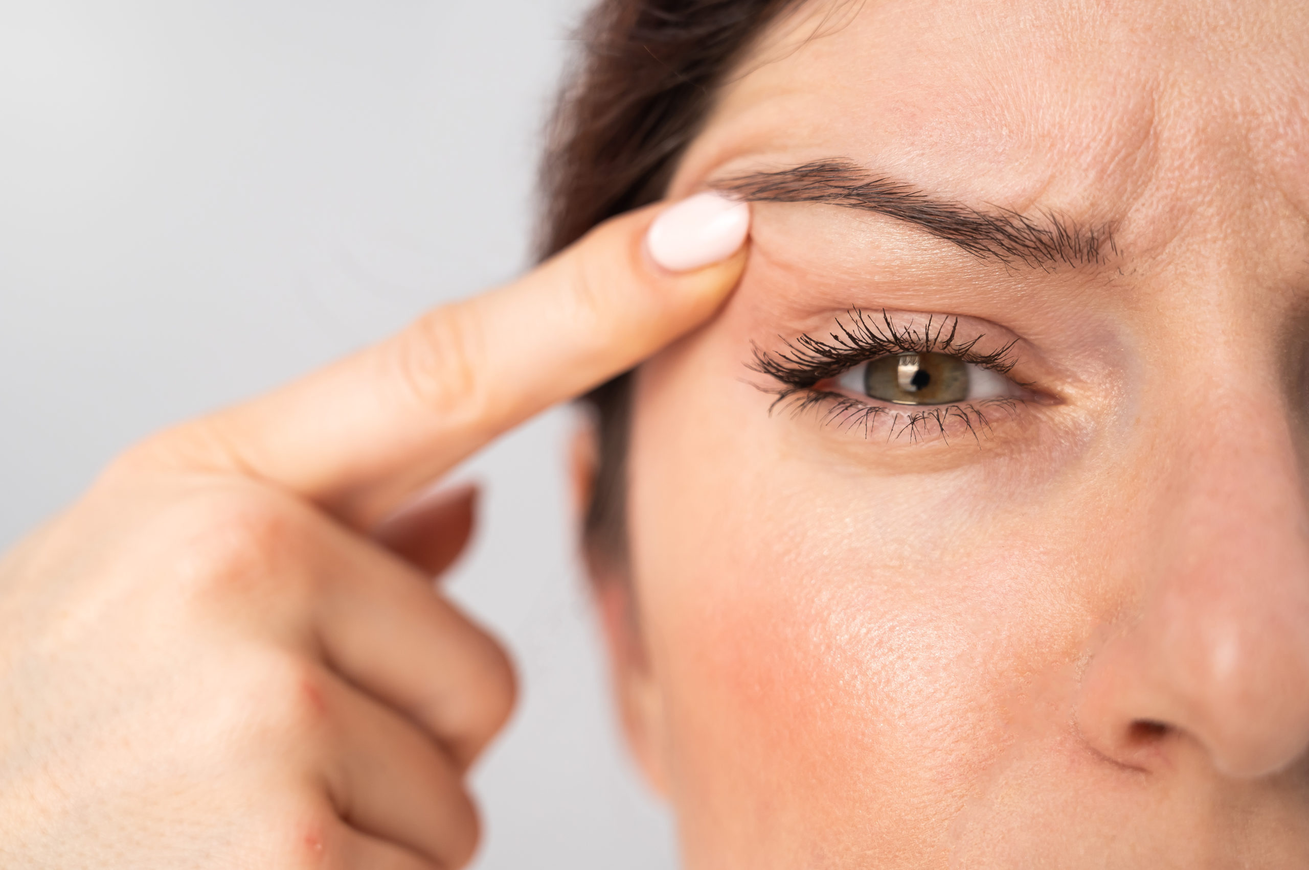 Close-up portrait of Caucasian middle-aged woman pointing to the wrinkles on the upper eyelid